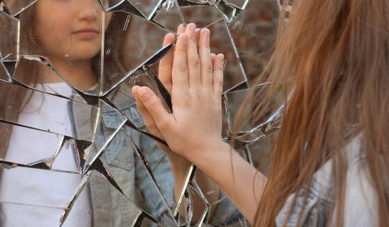 Girl looks in a broken mirror and shows her hand on a mirror.