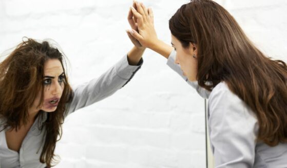 Attractive young woman looking in a mirror and seeing a hideous reflection.