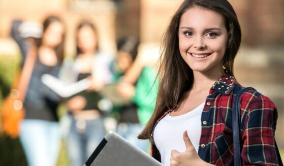 Young smiling female college student outdoors with classmates in the background.