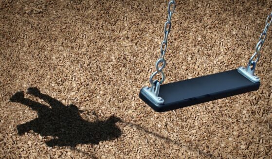 Missing child concept with empty playground swing and the shadow of a little girl on the park floor.