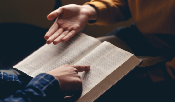 Male reading the Holy Bible and sharing with a friend. (pcess609/ Canva)