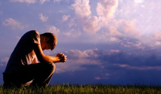 man kneeling in prayer under purple sky
