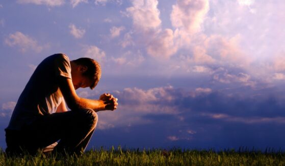 Young man praying on bended knee.