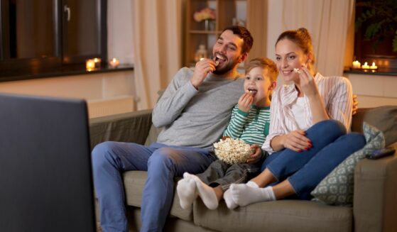 Happy family watching TV while eating popcorn indoors.