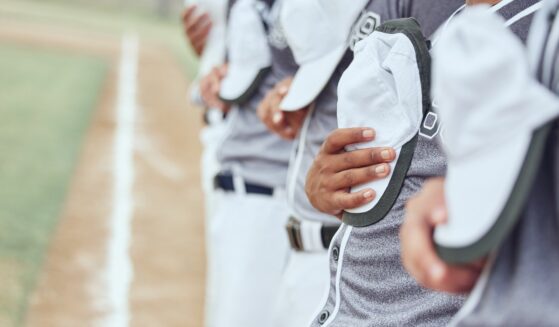 Closeup of baseball players with hats off, over their hearts, standing on the field in honor of the National Anthem.