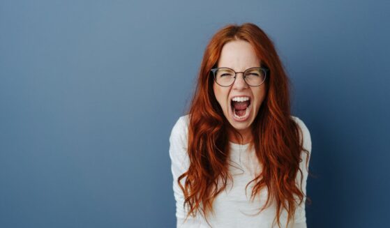 A young woman throwing a temper tantrum over a blue studio background.